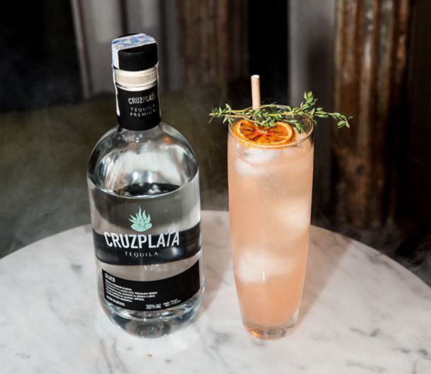 Una botella de tequila cruz plata junto a una bebida en una mesa.