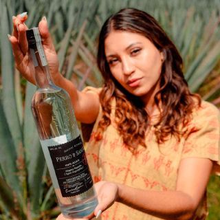Una mujer con una camisa amarilla sostiene una botella de tequila.