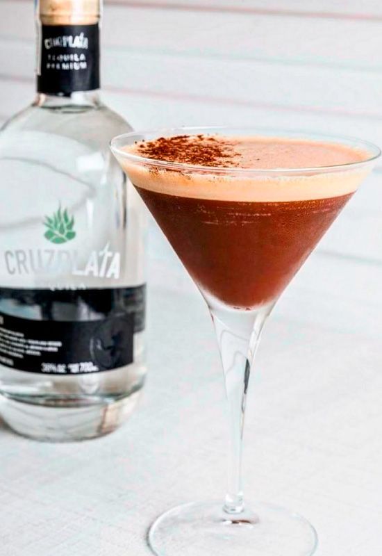 Un martini en una copa de martini junto a una botella de cruz plata