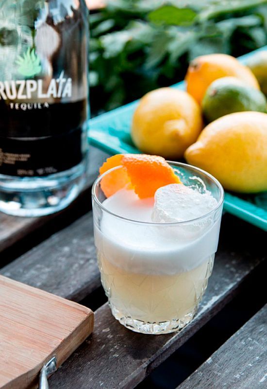 Una botella de tequila cruz plata junto a un vaso de bebida