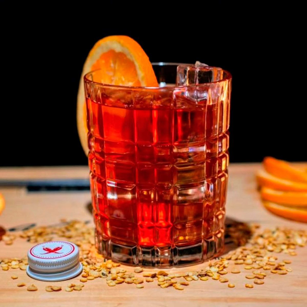Un vaso de líquido rojo con hielo y una rodaja de naranja encima.
