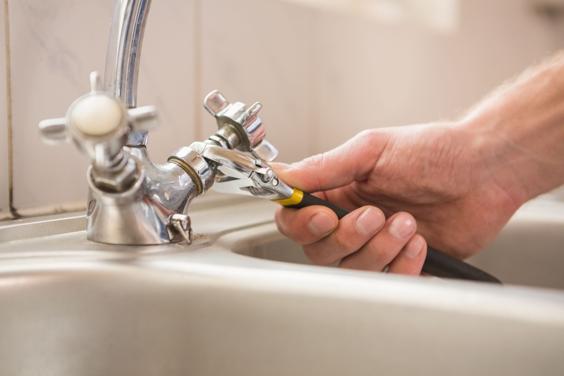 Un plombier utilisant une clef à molette sur un robinet de lavabo.