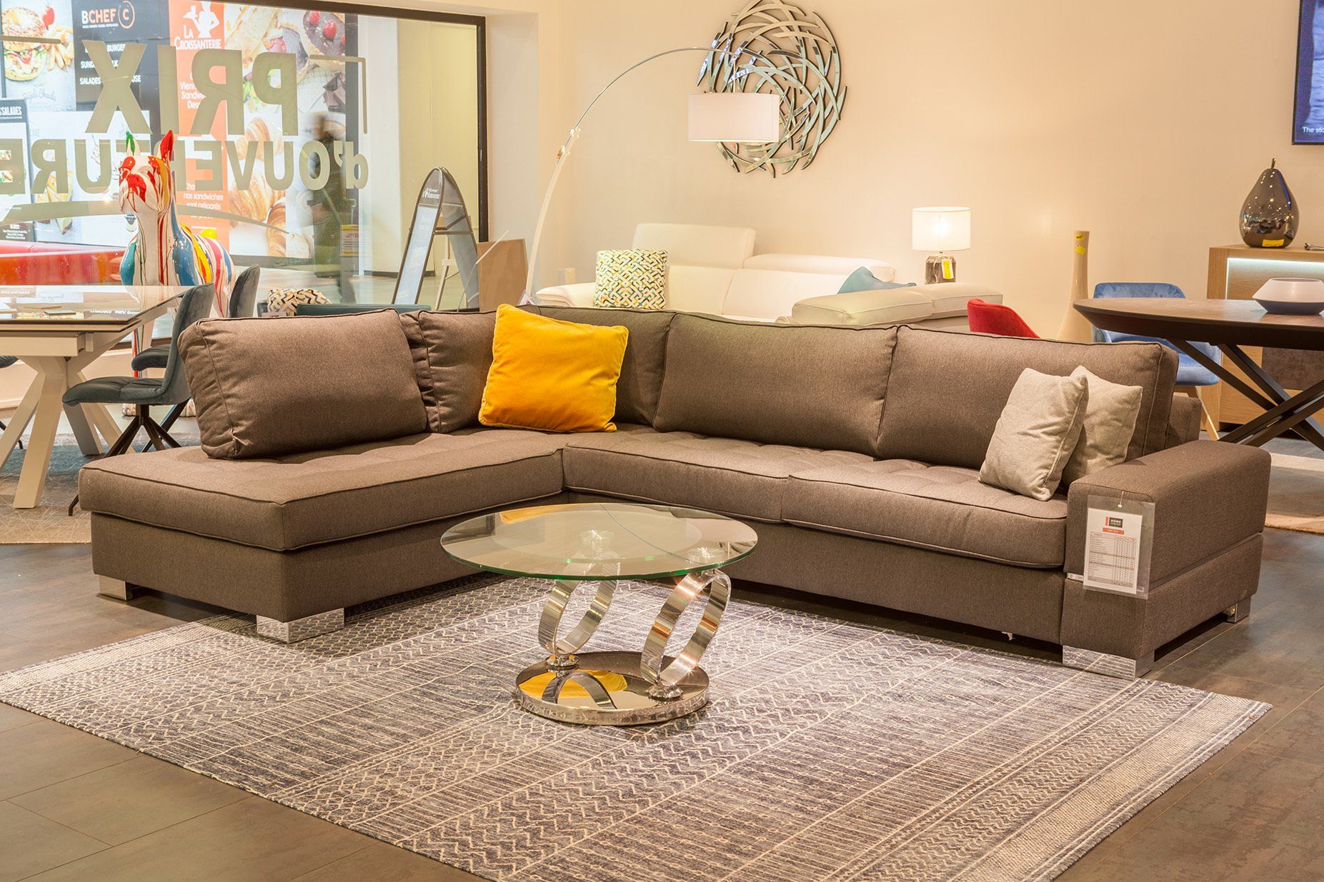 Canapé d'angle en tissu marron et oreiller jaune moutarde devant table basse ronde et tapis rectangulaire