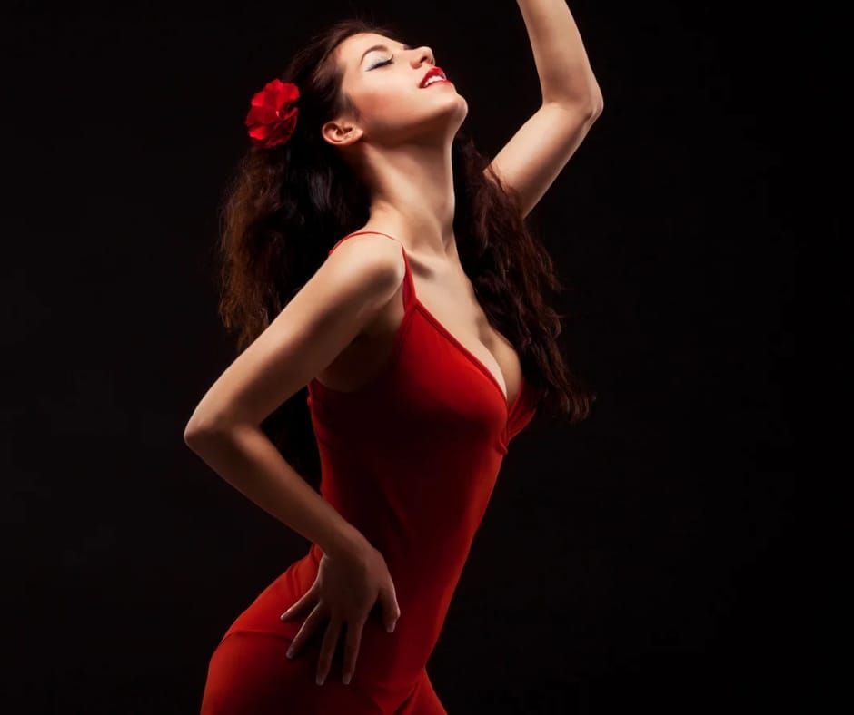 Mujer con vestido rojo baila, brazo levantado, flor en el pelo, fondo oscuro.