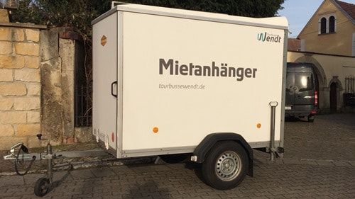 Ein weißer Anhänger mit der Aufschrift „Mietanhänger“ steht auf einem Parkplatz.