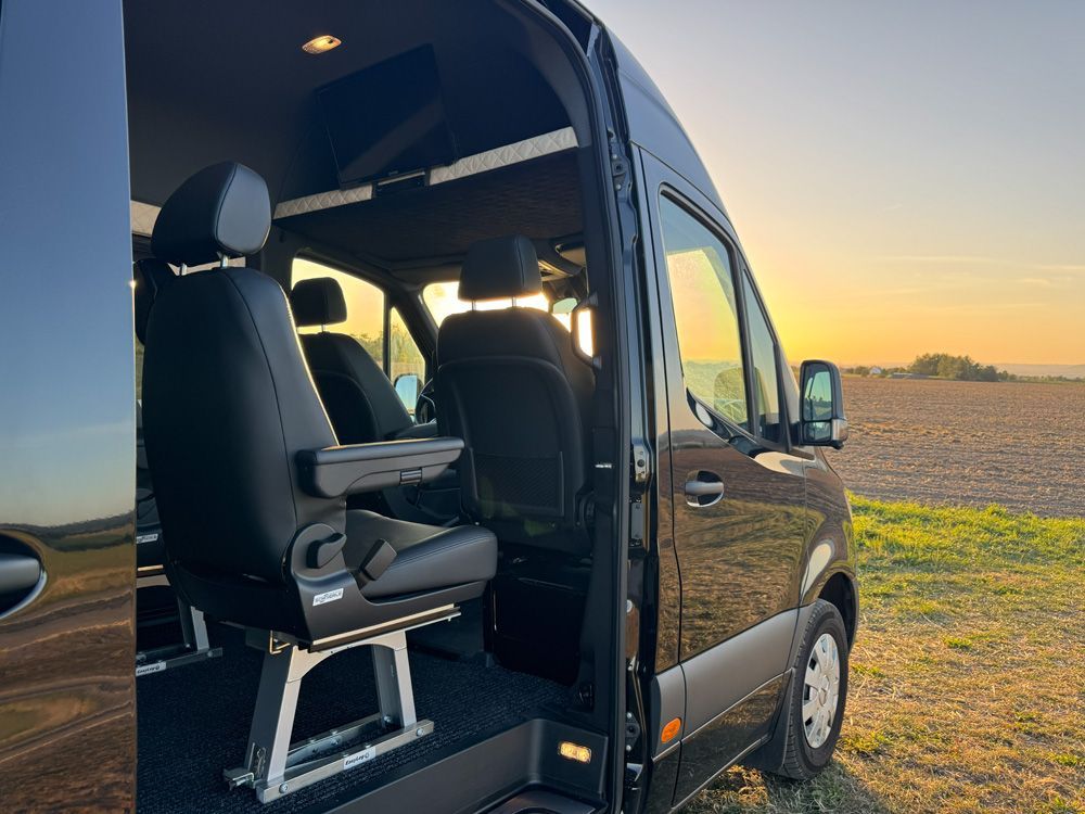 Rollstuhllift in einem schwarzen Lieferwagen bei Sonnenuntergang, geparkt neben einem offenen Feld.