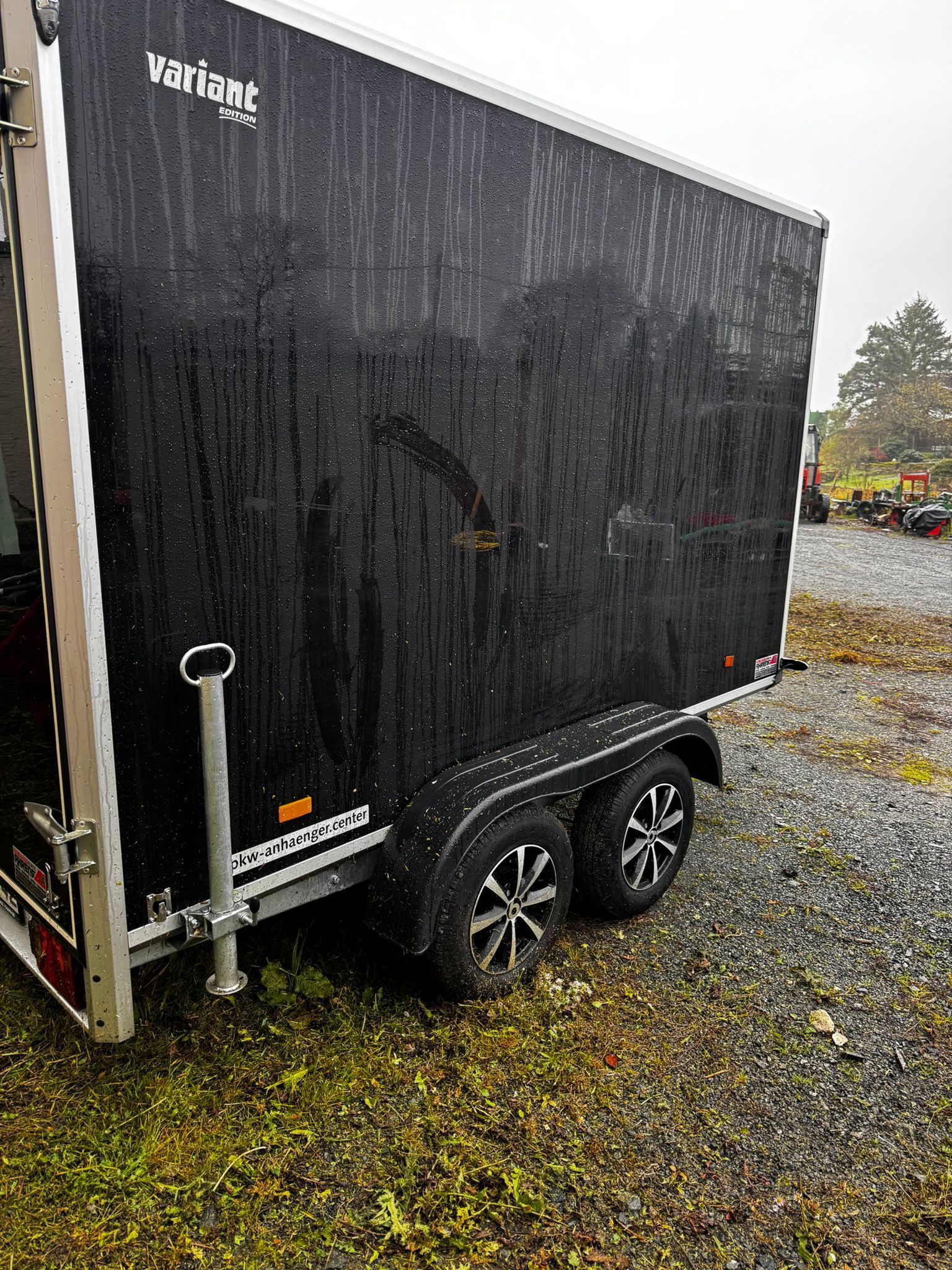 Ein schwarzer Anhänger steht auf einem Schotterplatz.