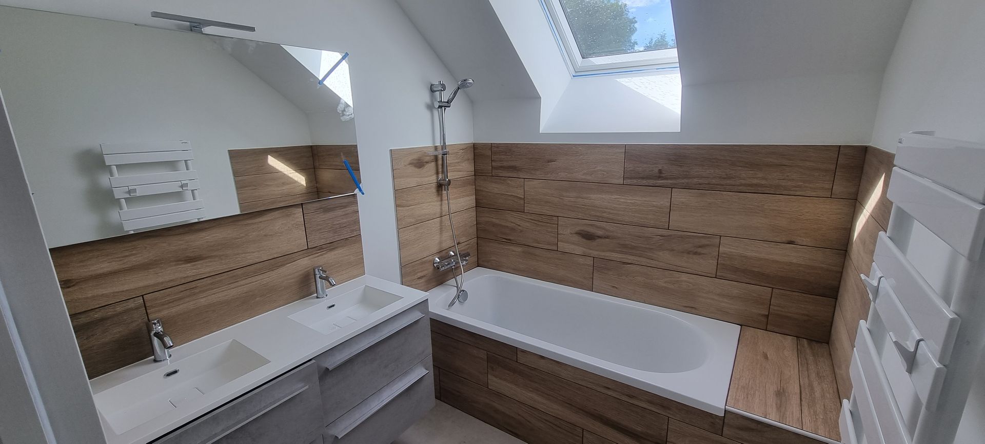 Salle de bains avec lambris, baignoire et double vasque sous un puits de lumière.