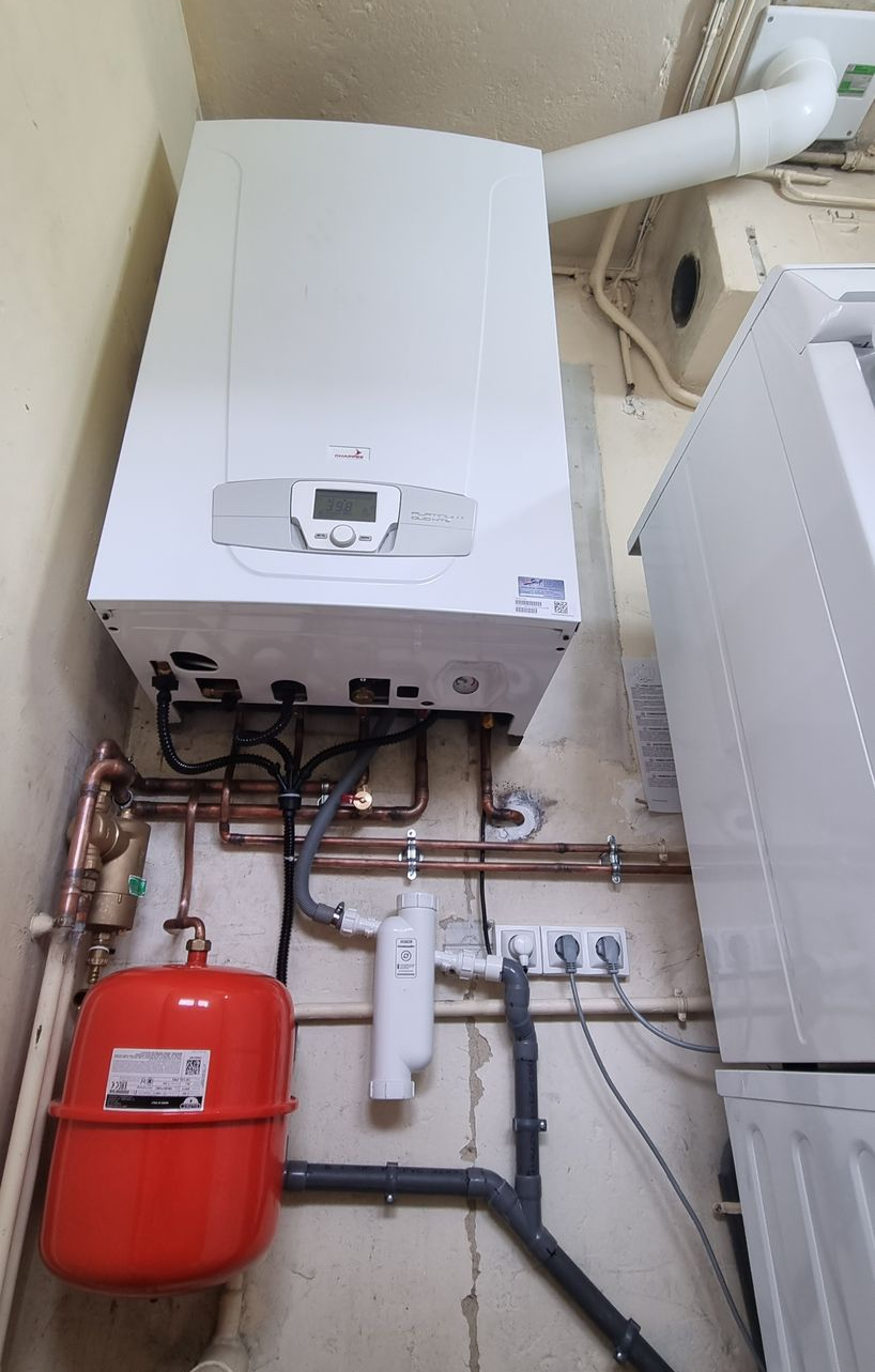 Chaudière à gaz blanche, tuyaux en cuivre, vase d'expansion rouge et filtre à eau mural.