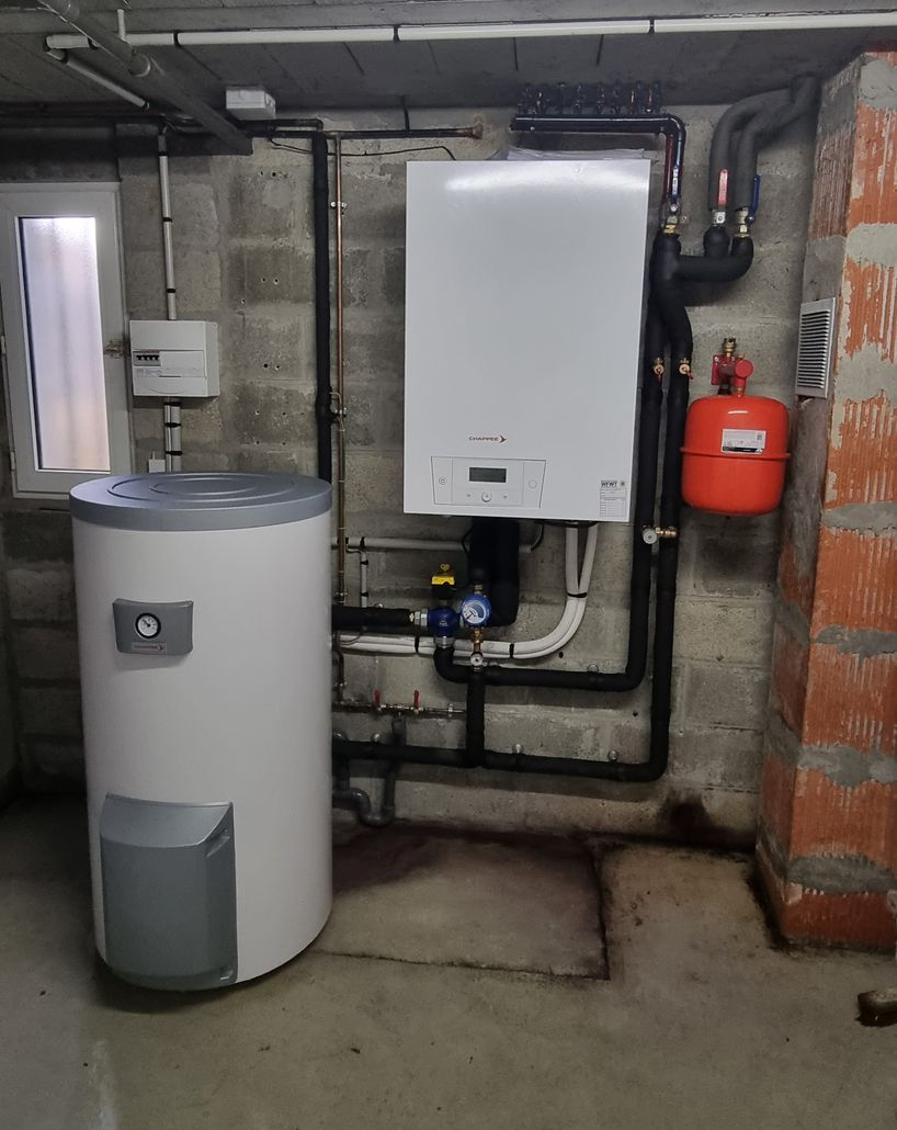 Chauffe-eau et chaudière avec tuyauterie au sous-sol. Appareils blancs, réservoir rouge, murs gris.