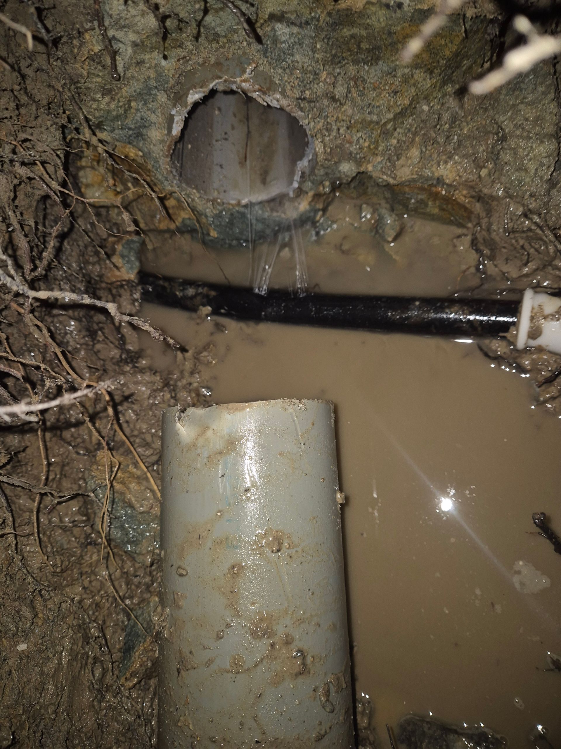 Fuite de tuyau dans un trou boueux. L'eau s'écoule d'une section endommagée et forme une flaque dans le sol.