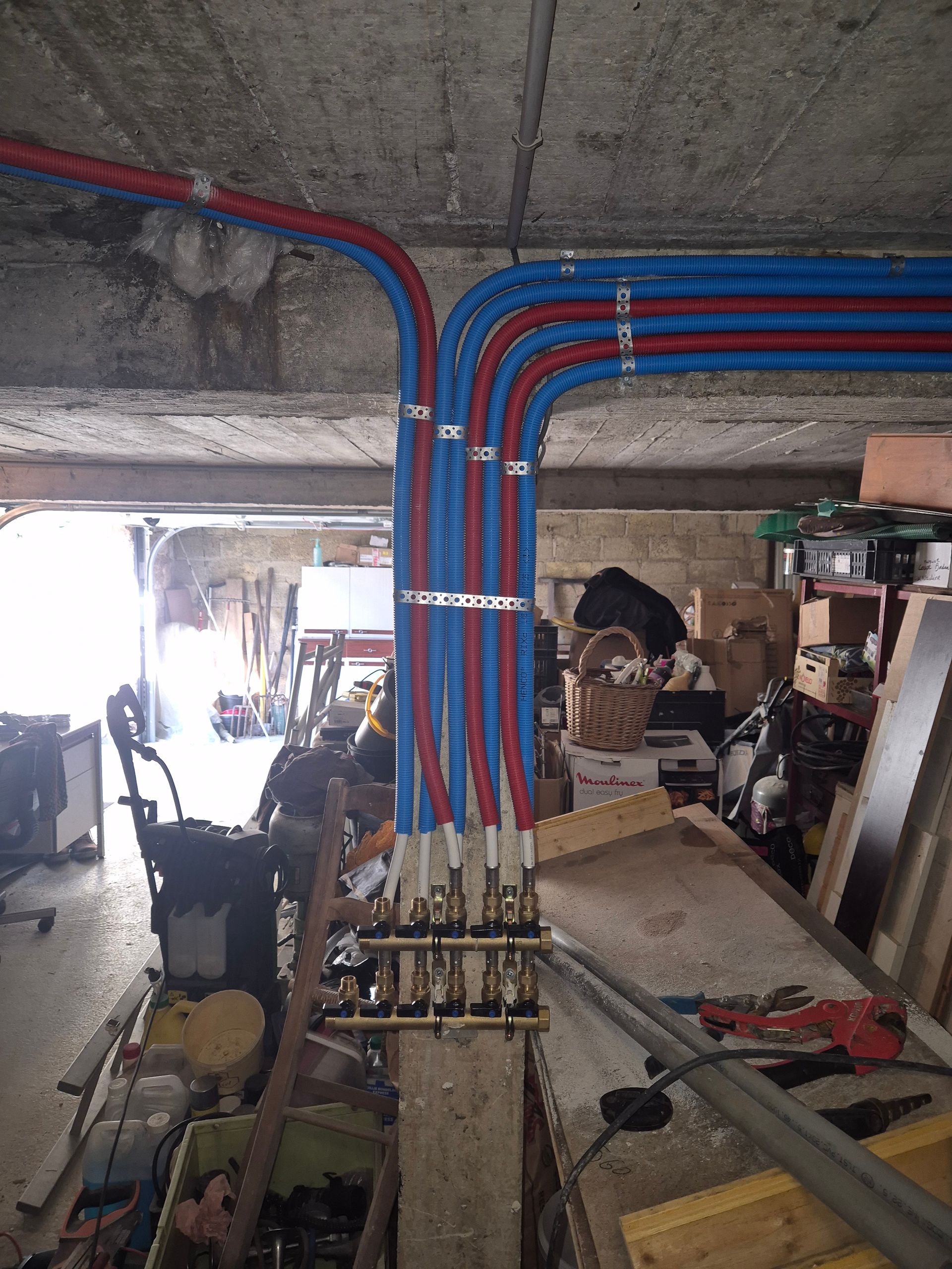 Des tuyaux, principalement bleus et rouges, raccordés à un collecteur dans un espace ressemblant à un garage.
