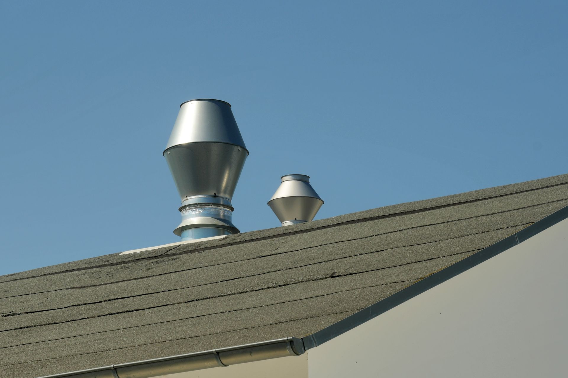 Deux grilles d'aération métalliques sur un toit gris se détachant sur un ciel bleu limpide.
