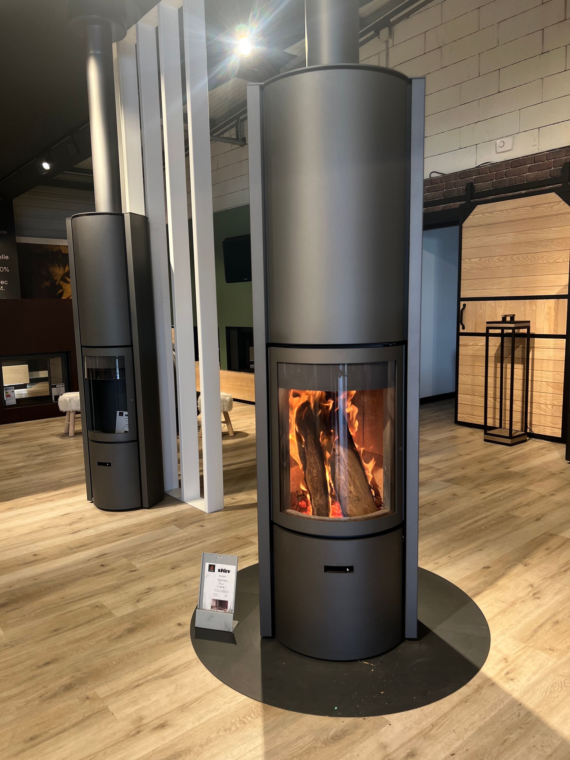 Deux cheminées modernes grises avec des flammes qui brûlent, dans une salle d'exposition avec parquet.