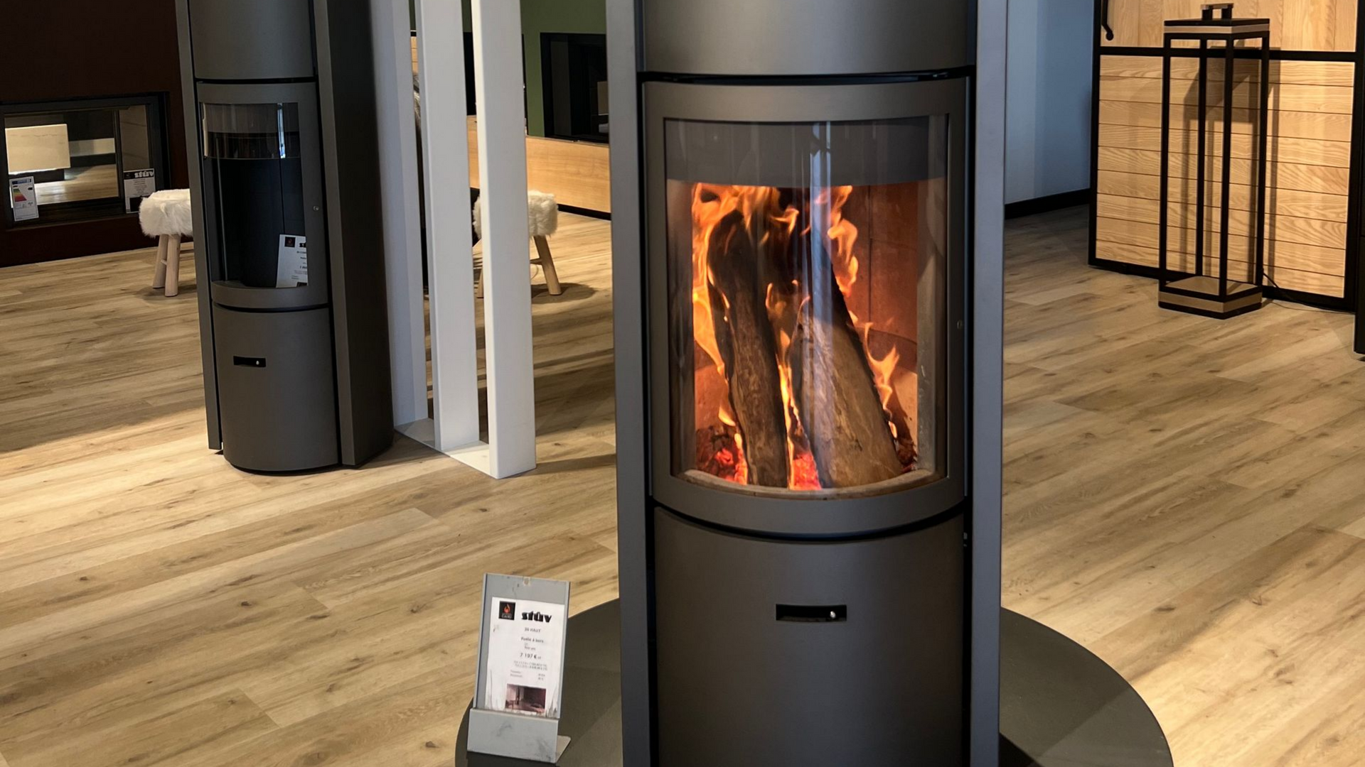 Poêle à bois cylindrique couleur anthracite, avec un feu incandescent visible à travers une porte vitrée.