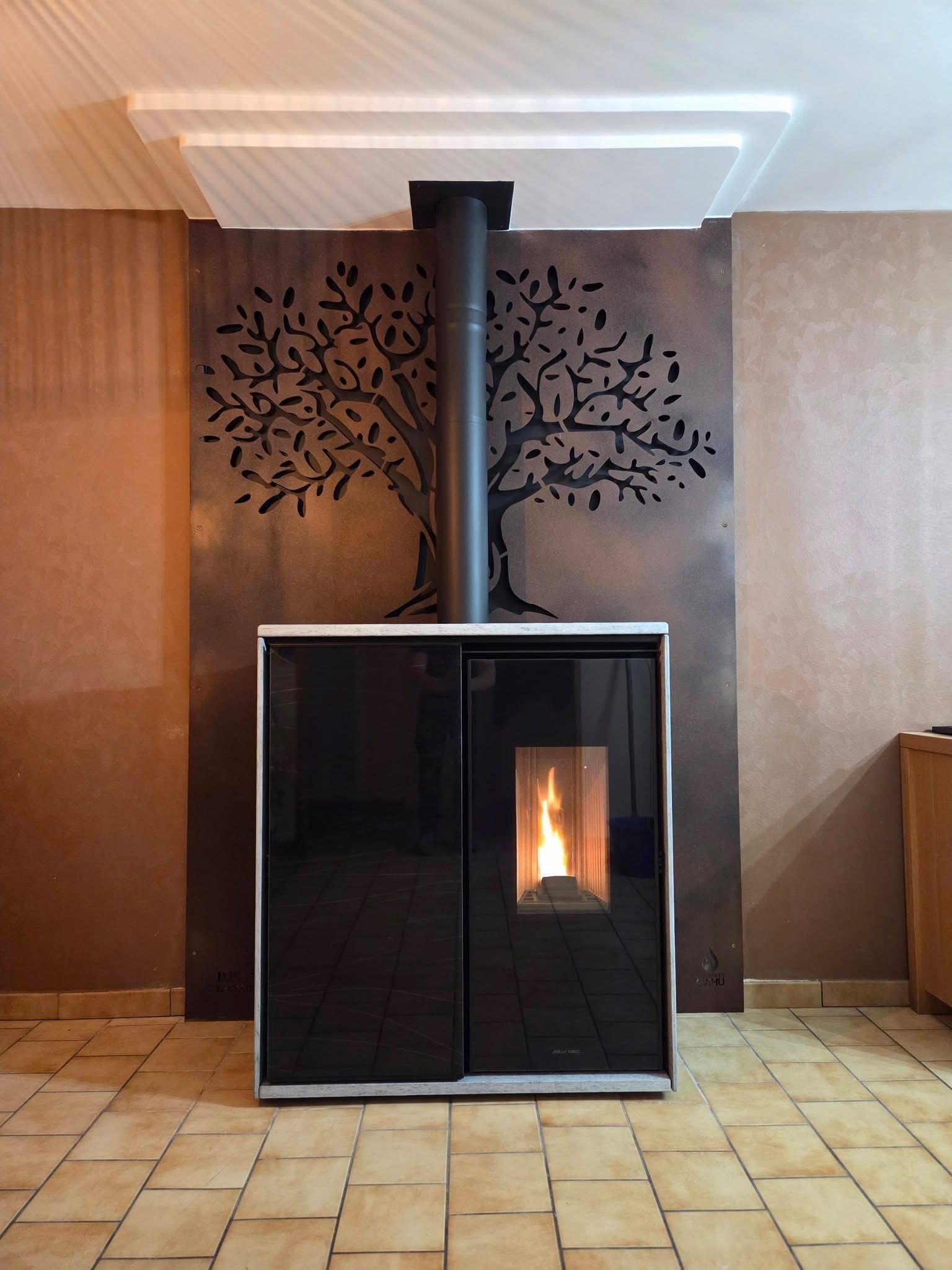 Cheminée noire moderne avec une flamme, contre un mur en cuivre orné d'une silhouette d'arbre, avec un conduit noir.