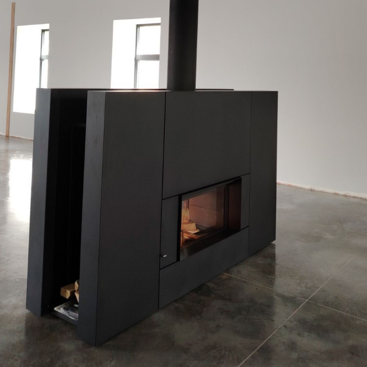 Cheminée moderne noire dans une pièce, avec bûches dans le compartiment latéral, conduit de cheminée.