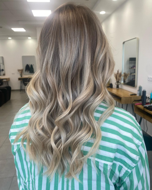 Femme aux cheveux ondulés avec des mèches blondes, dans un salon de coiffure.