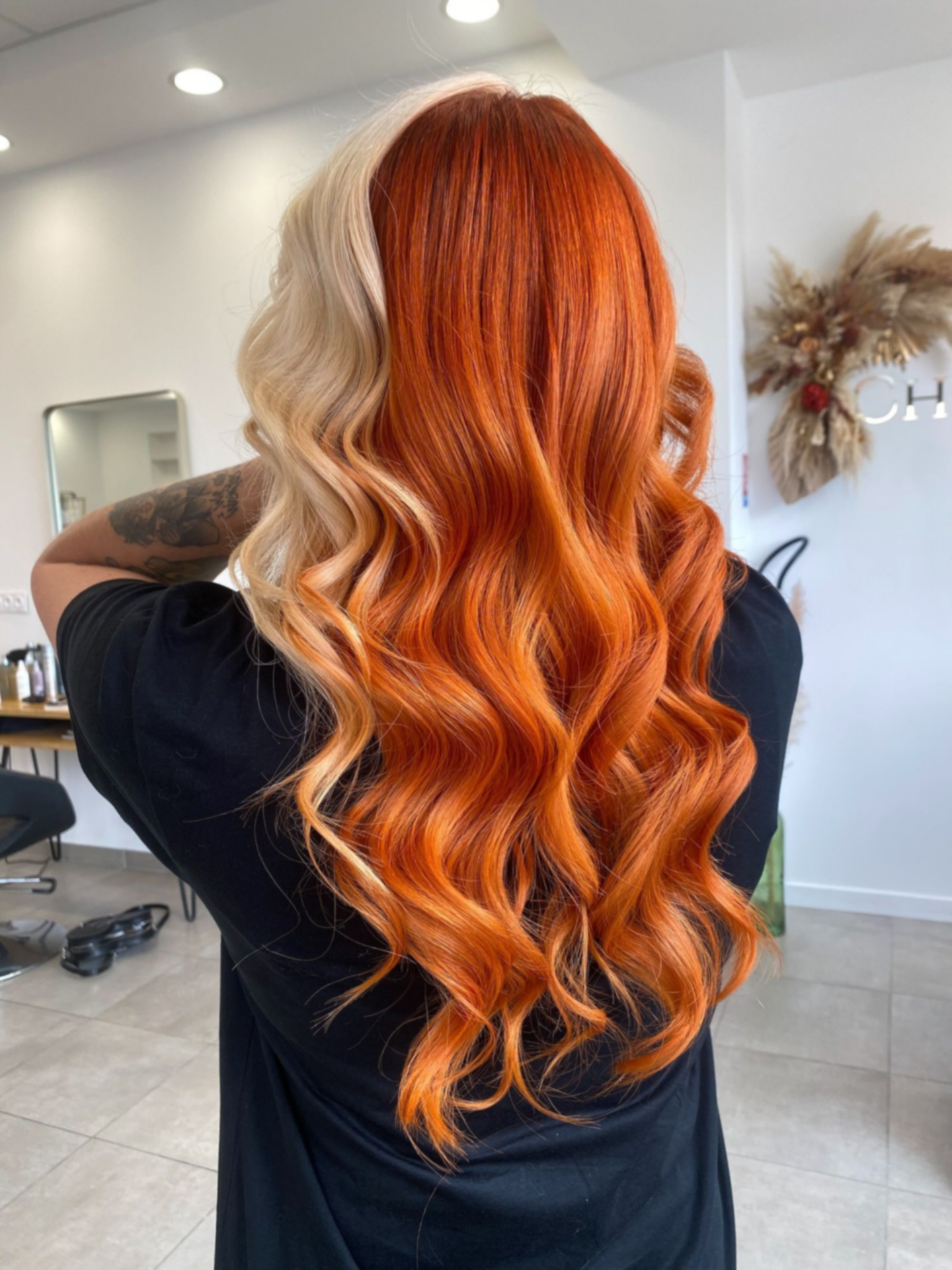 Femme aux longs cheveux coiffés en deux couleurs, blond et orange, avec des boucles lâches.