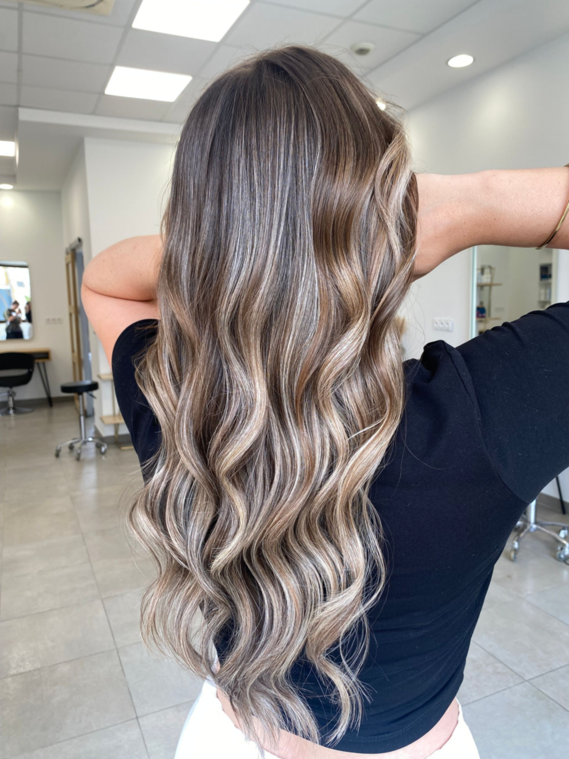 Femme aux cheveux ondulés avec des mèches blondes, dans un salon de coiffure.