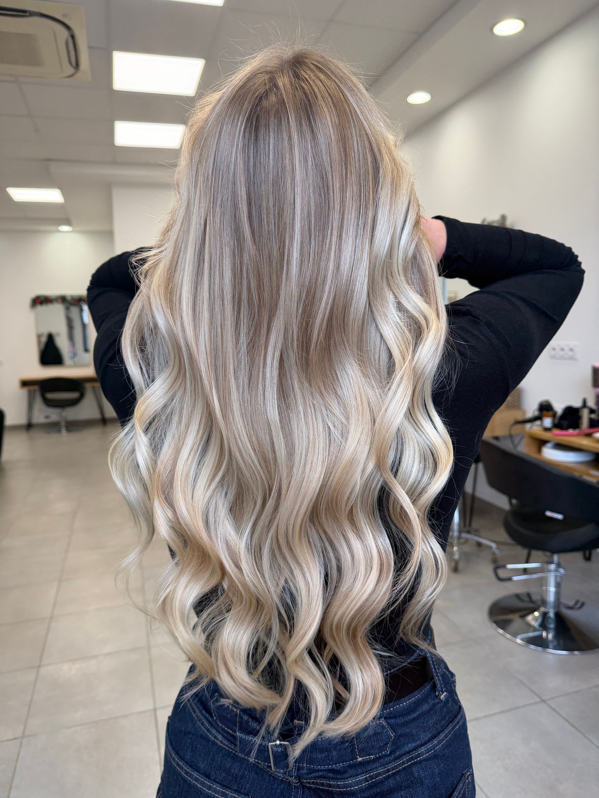 Cheveux longs, bruns et ondulés avec des mèches, vus de dos, dans un salon de coiffure bien éclairé.