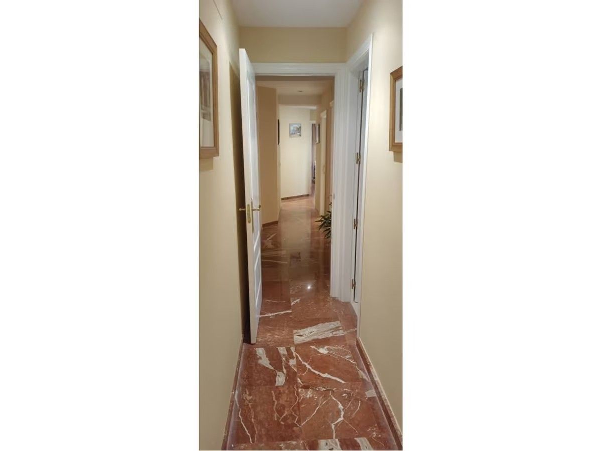 Un largo pasillo con suelo de mármol y una puerta que conduce a una habitación.