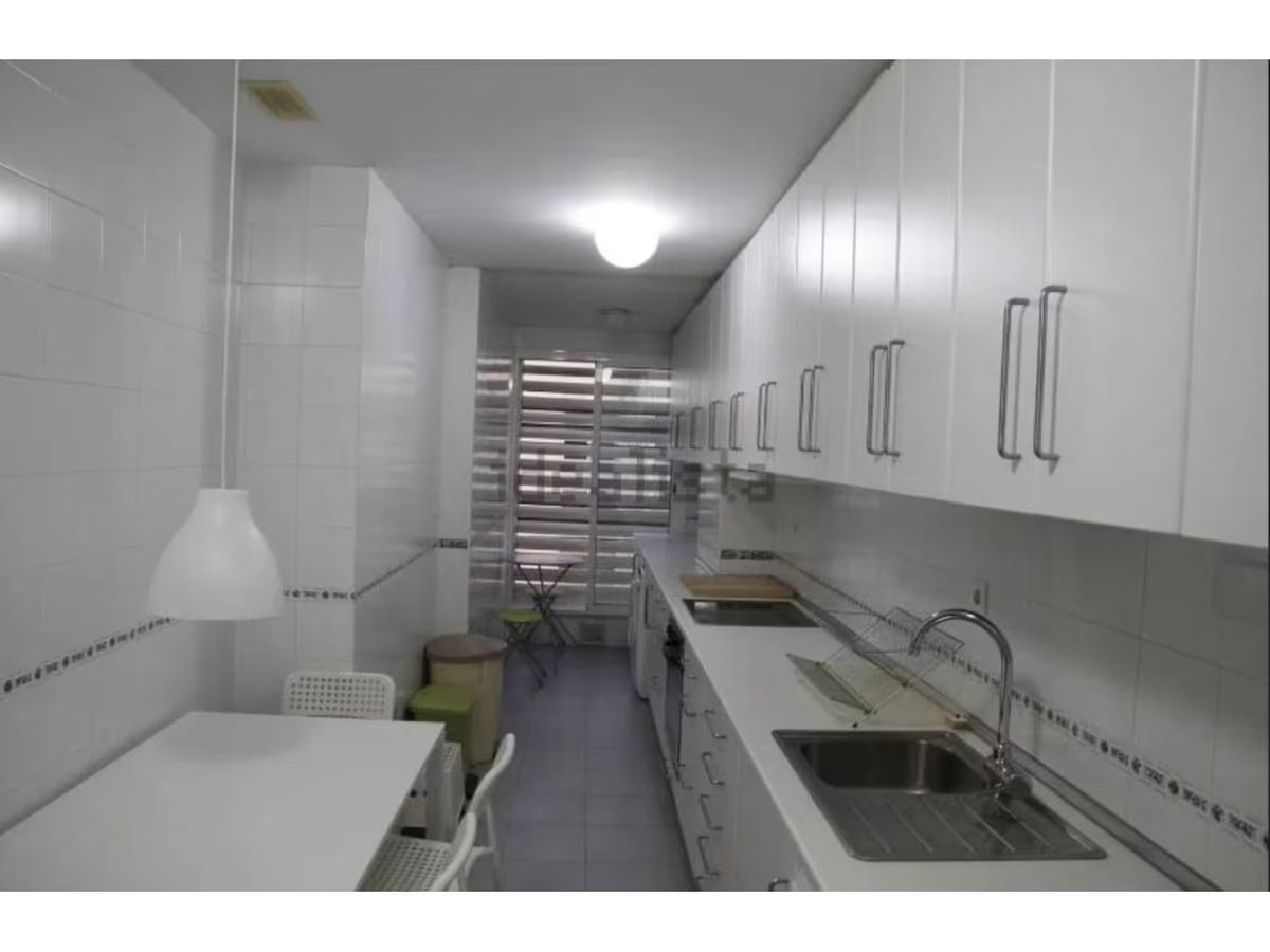 Una cocina larga con gabinetes blancos y un fregadero.