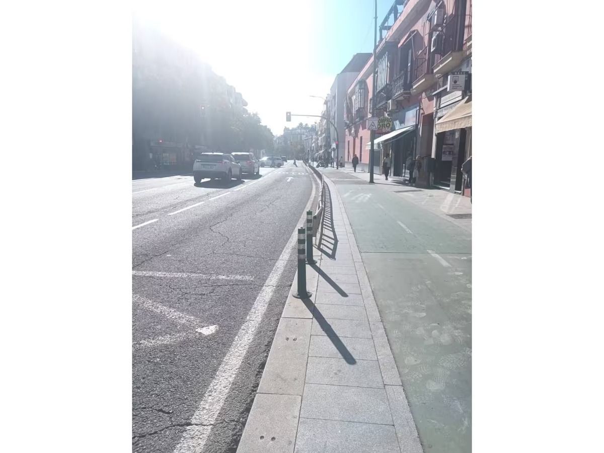 Una calle con un banco al costado y autos circulando por ella.