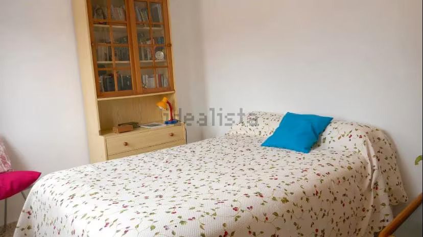 Una cama con una manta floral y una almohada azul en un dormitorio.