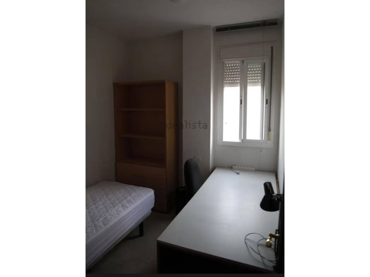 Un dormitorio con cama, escritorio, estantería y ventana.