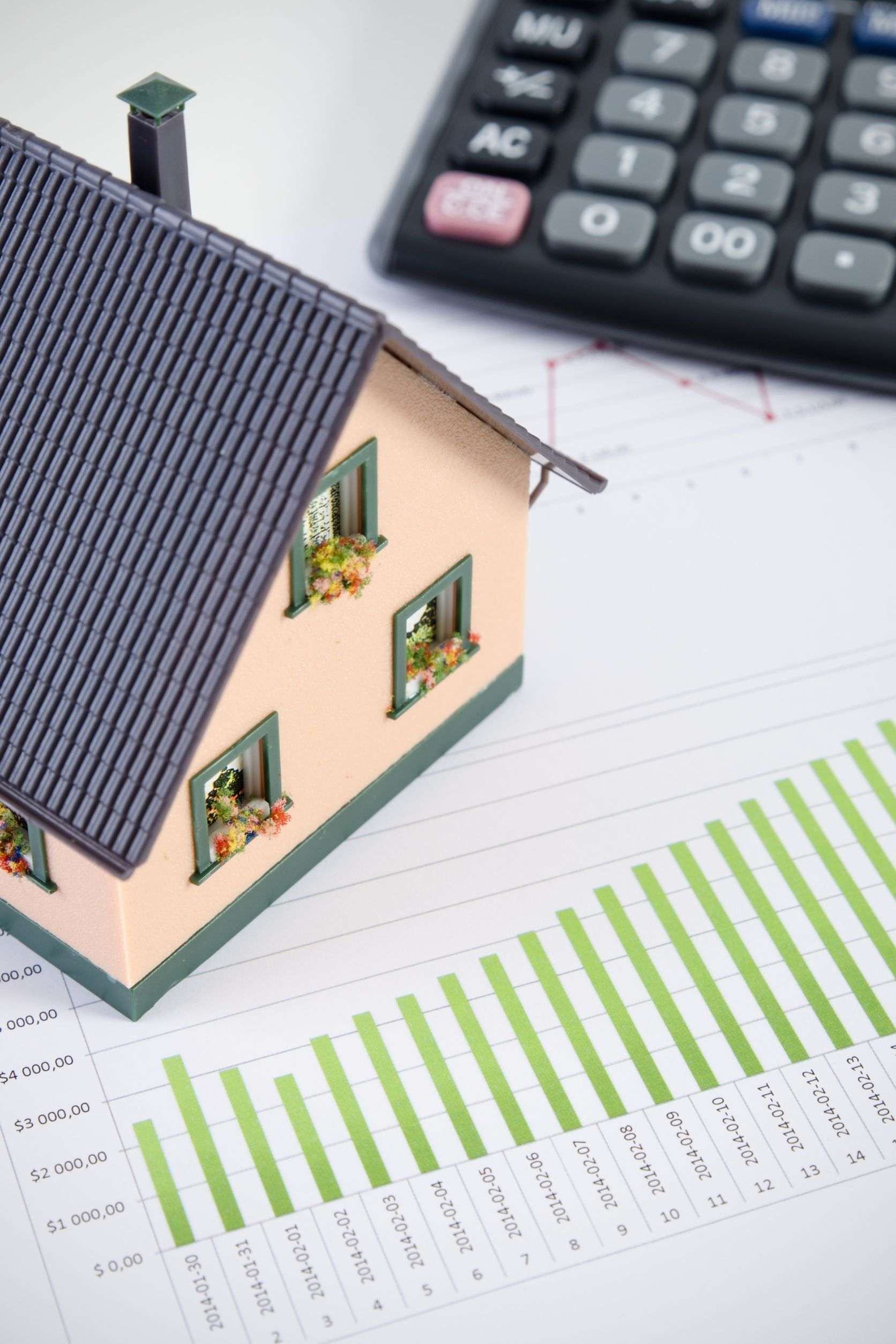 Una casa modelo está colocada encima de un gráfico al lado de una calculadora.