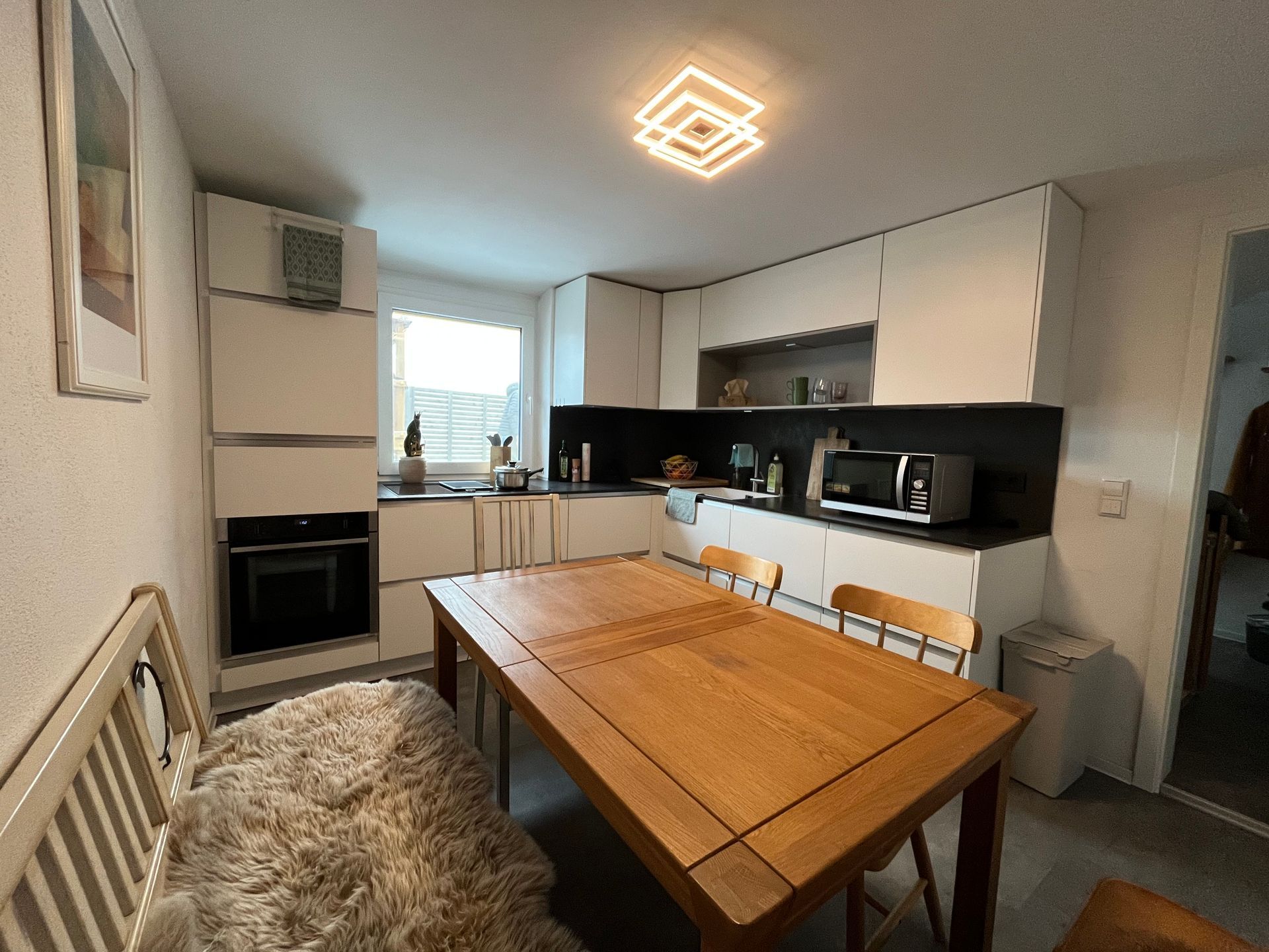 Küche mit weißen Schränken, Holztisch und Bank mit einem flauschigen Schaffell.