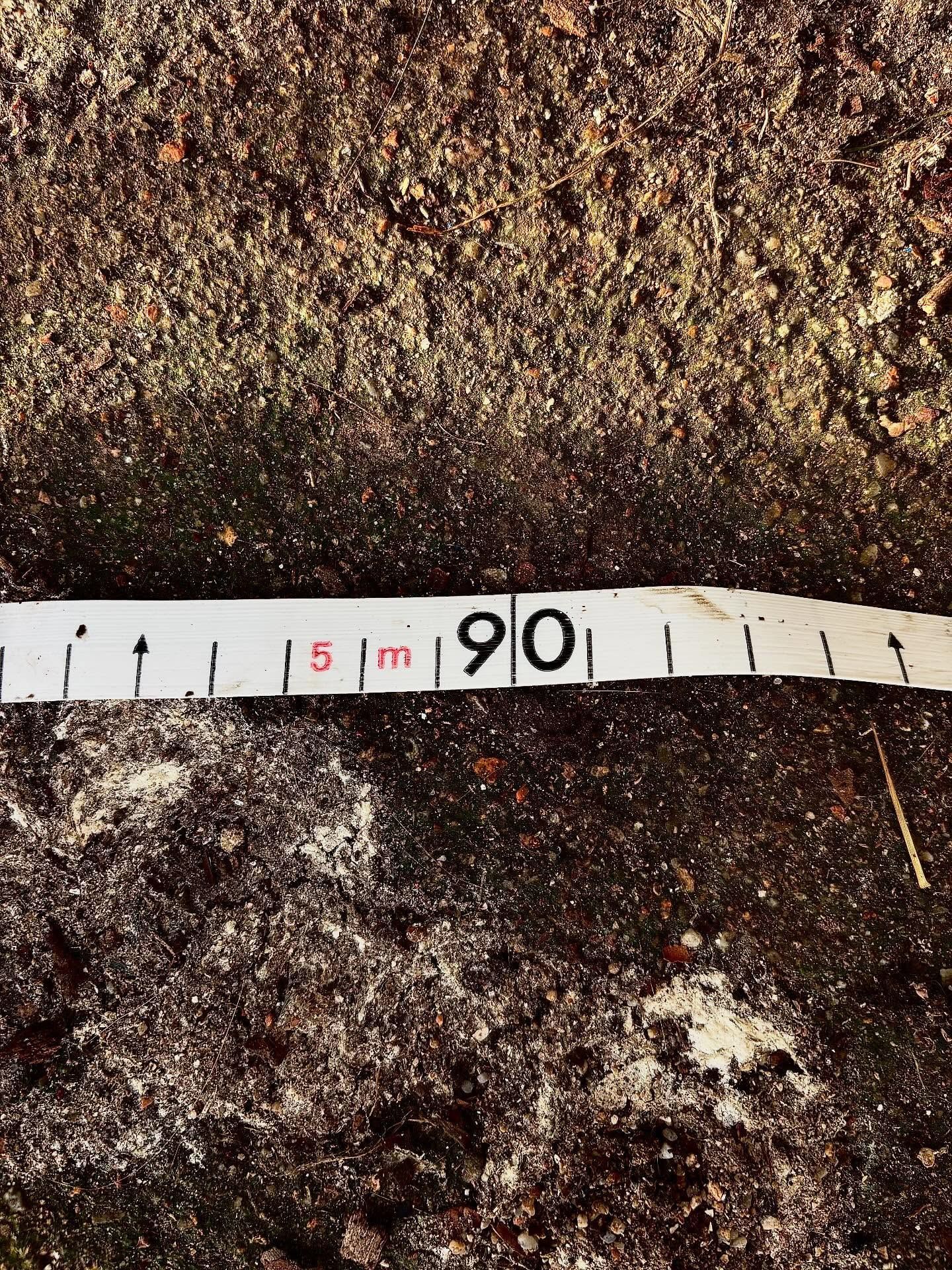 Un mètre ruban posé sur un sol irrégulier, avec les graduations autour de 90 cm.