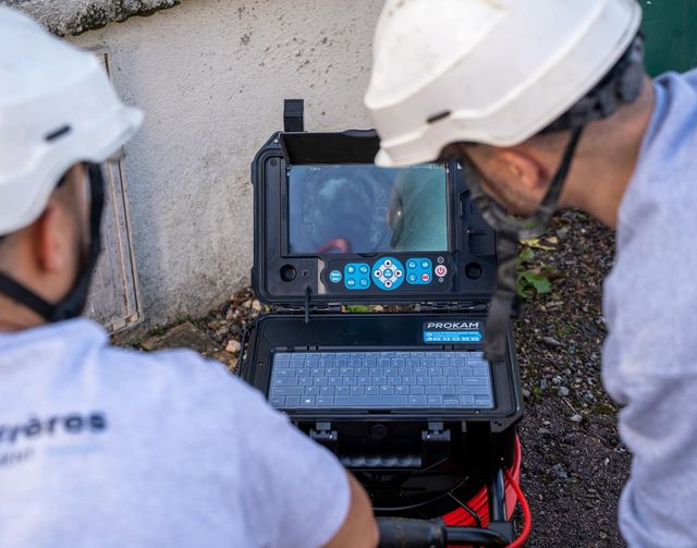 Deux ouvriers casqués inspectent un ordinateur portable et un écran sur un chantier.