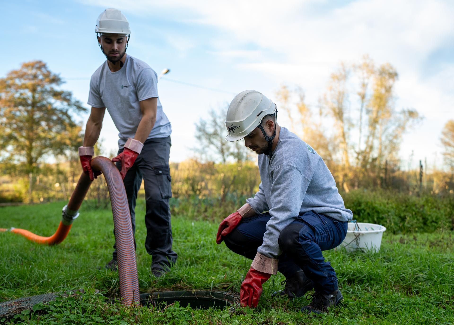 Deux ouvriers portant des casques de chantier effectuent le pompage d'une canalisation.