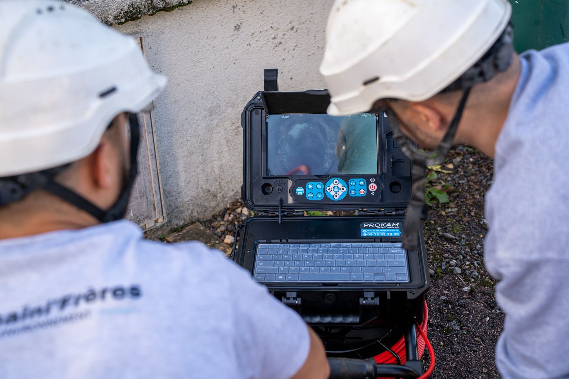Deux ouvriers inspectent un ordinateur portable relié à une caméra d’inspection des réseaux électriques en plein air.