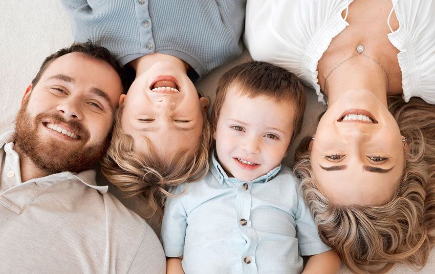 Una familia está acostada de espaldas en una cama y sonríe a la cámara.