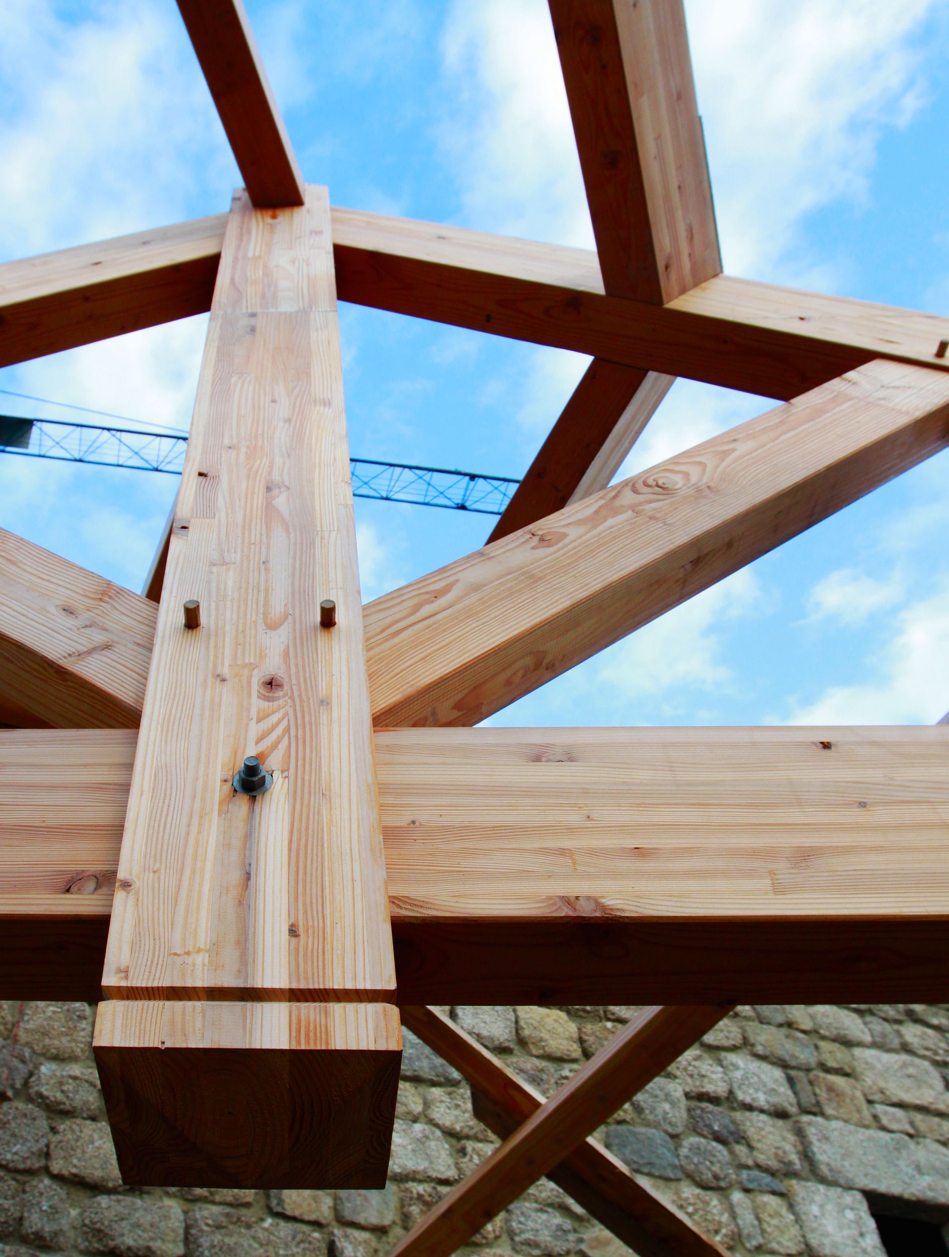 Charpente de toit en bois se détachant sur un ciel bleu, reliée par de grosses poutres en bois et des poteaux de soutien verticaux.