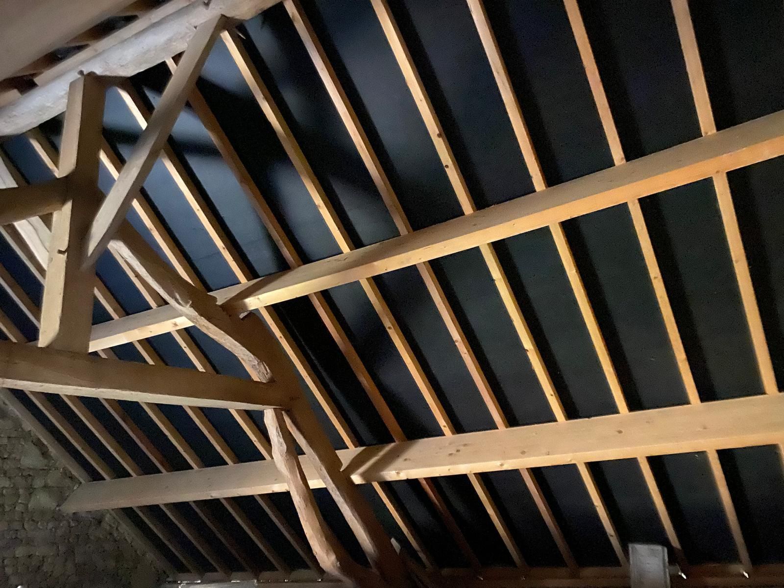 Charpente en bois avec isolation noire dans un grenier.