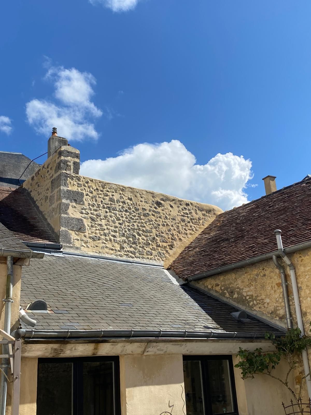 Toits et murs de pierre se détachant sur un ciel bleu éclatant parsemé de nuages ​​blancs cotonneux.