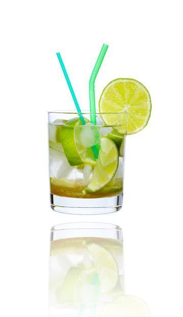 Cóctel en vaso con limas, hielo y pajitas; reflejado debajo.