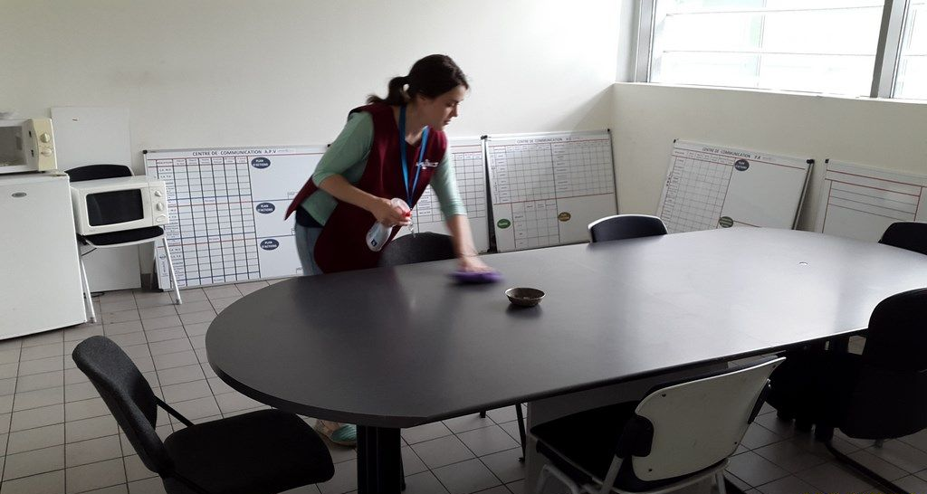 Une employée nettoie une grande table noire.