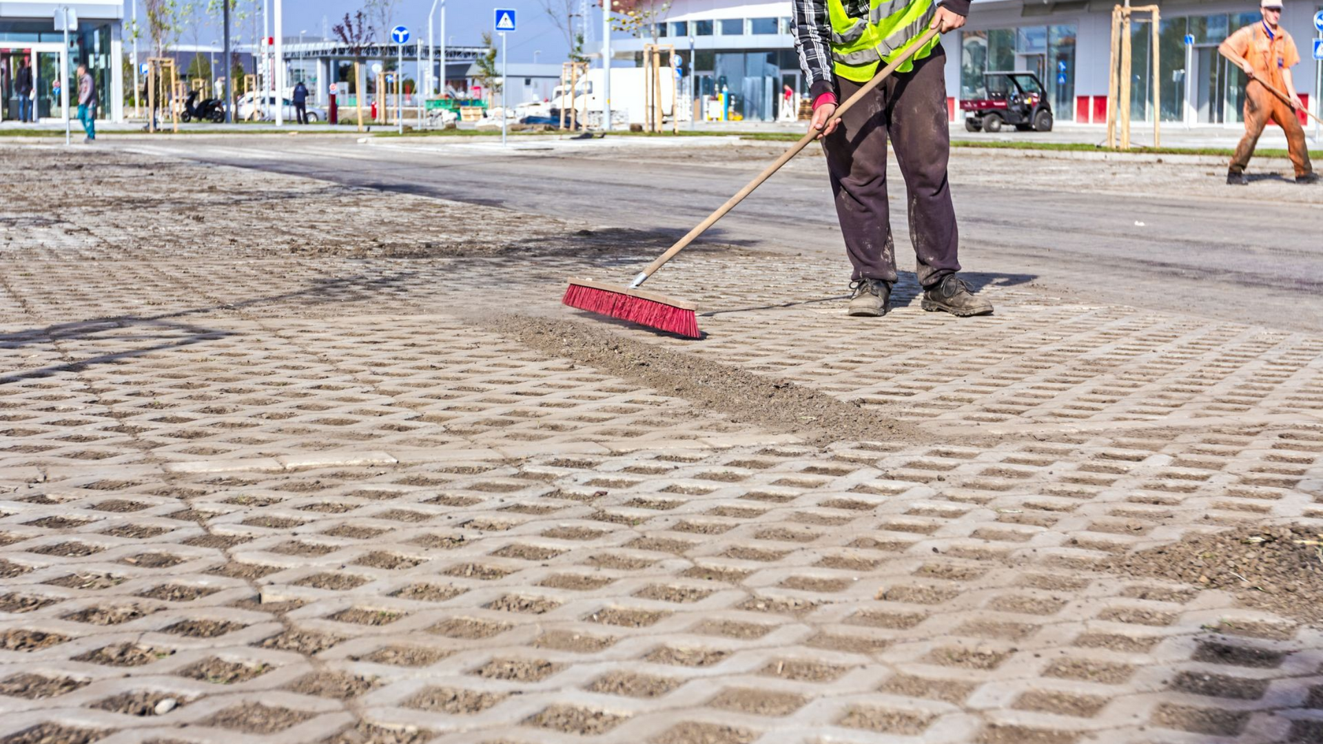 Un employé nettoie un parking avec un balai rouge.