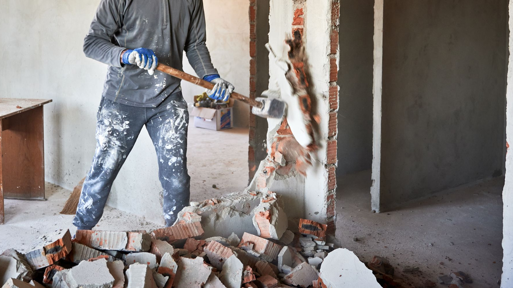 Un ouvrier démolit un mur en brique à l'aide d'une masse.