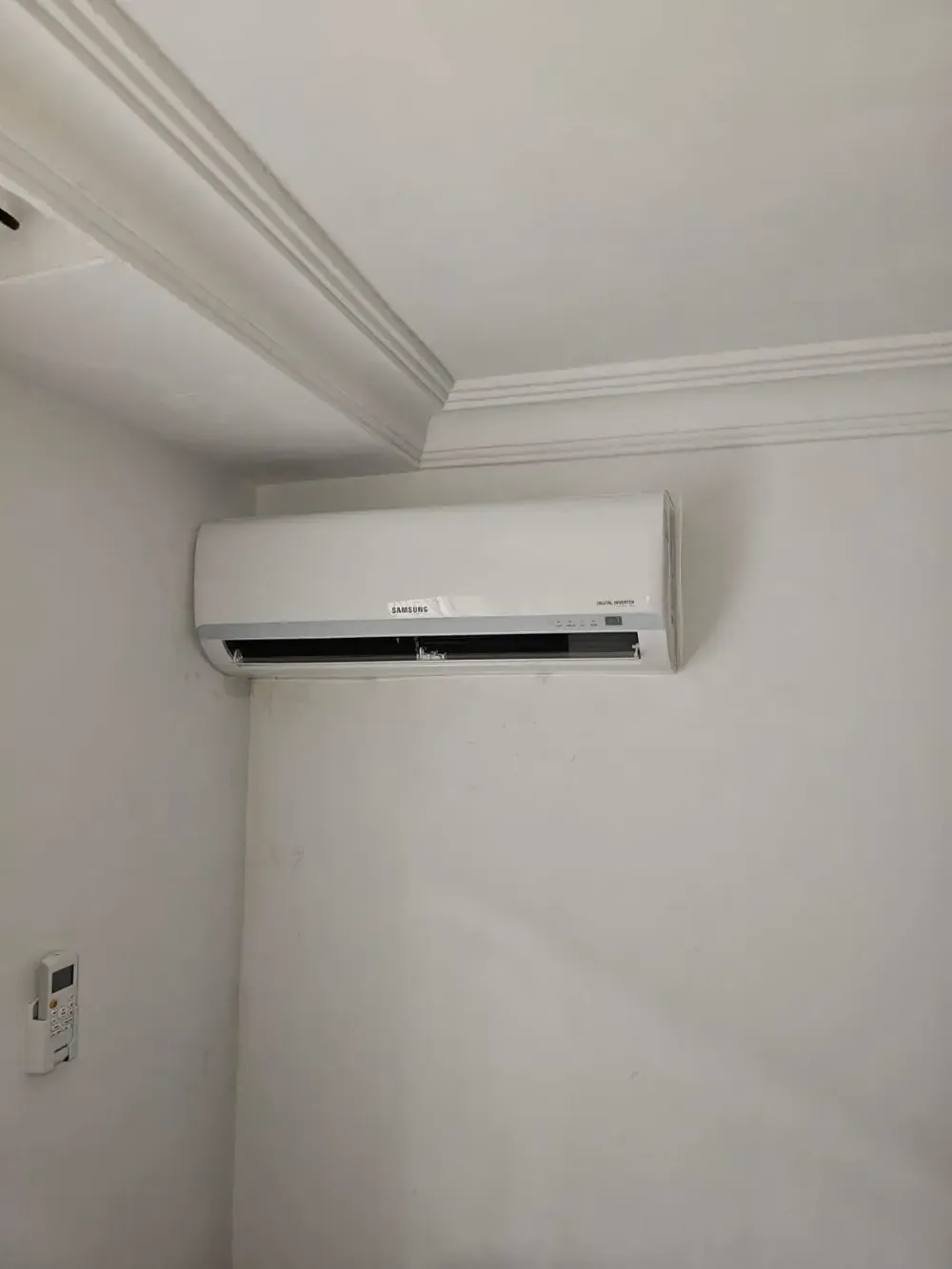 Aire acondicionado blanco de pared, cerca del techo, en una habitación sencilla