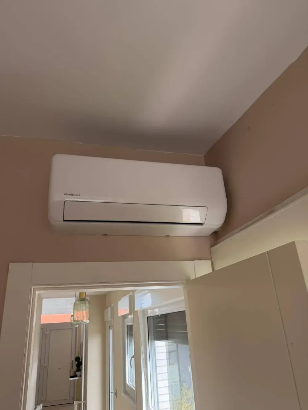 Aire acondicionado blanco de pared encima de una puerta en una habitación beige