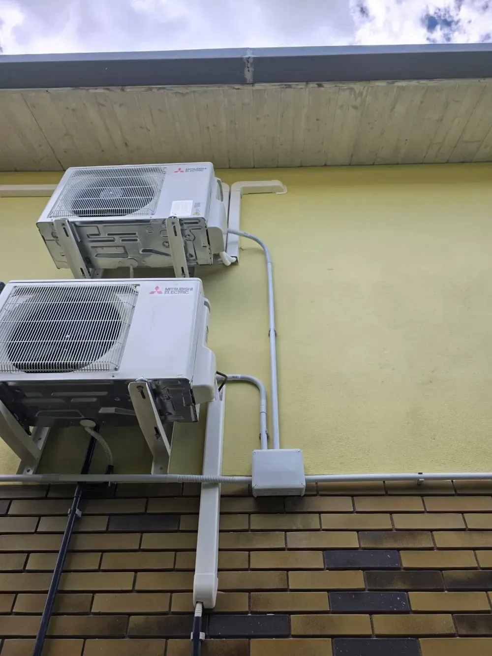 Dos aires acondicionados de pared con las tuberías a la vista en una fachada de ladrillo amarillo