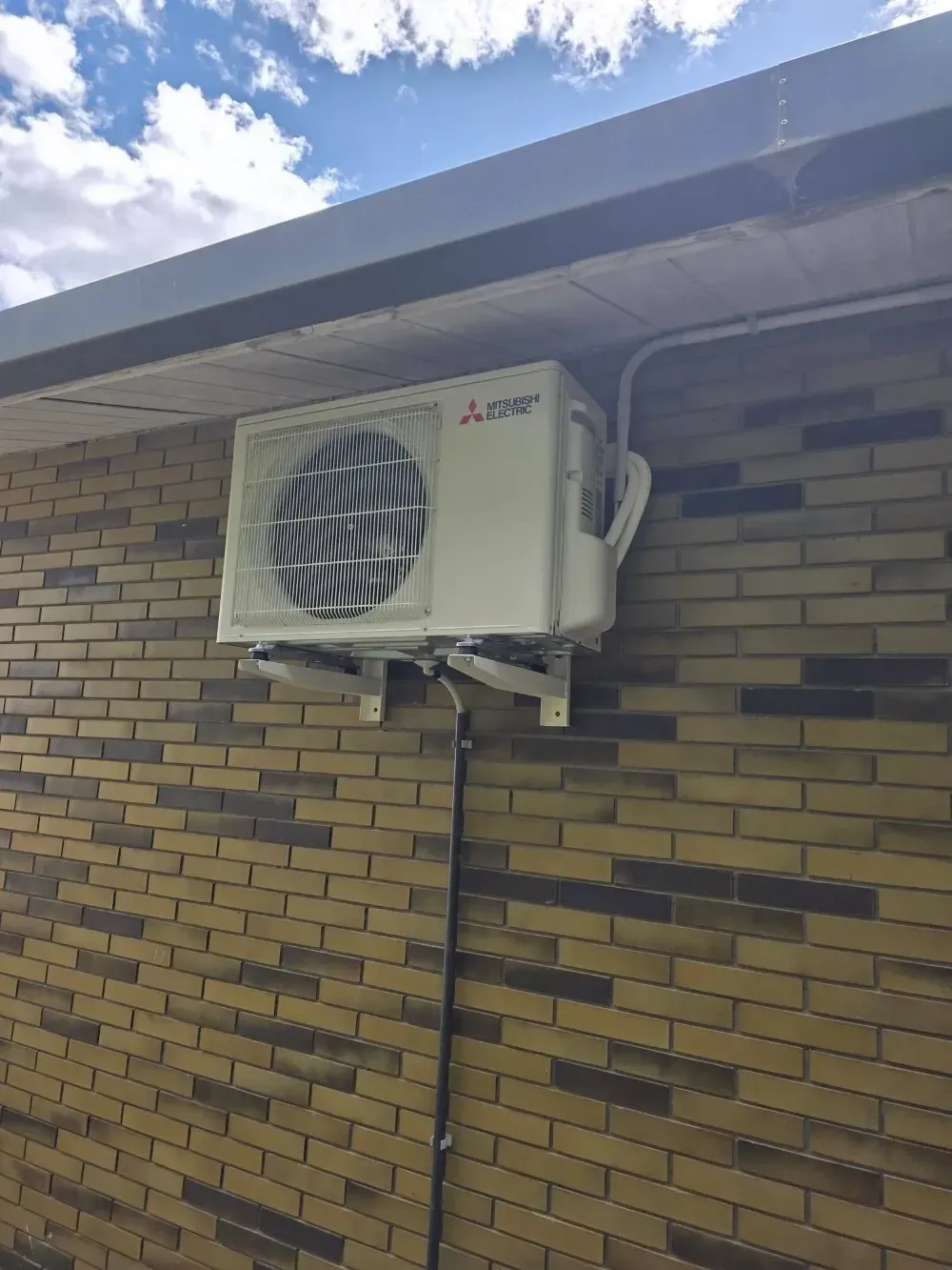 Aire acondicionado de pared en un edificio de ladrillo bajo un cielo nublado.
