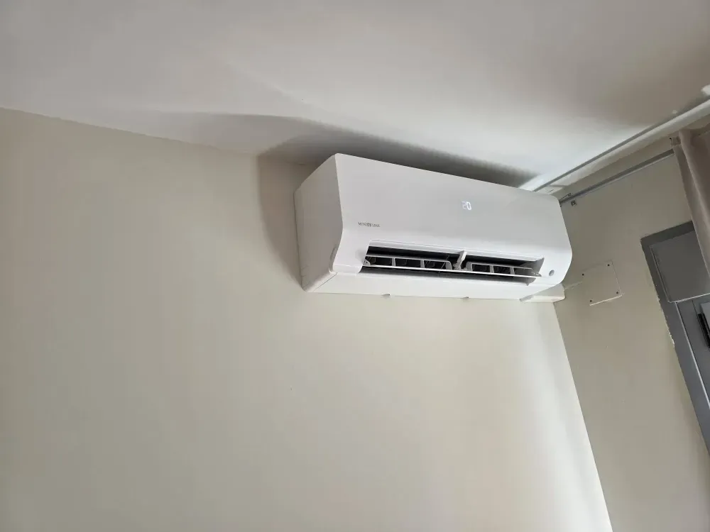 Aire acondicionado blanco instalado en la pared, cerca del techo, en una habitación sencilla.