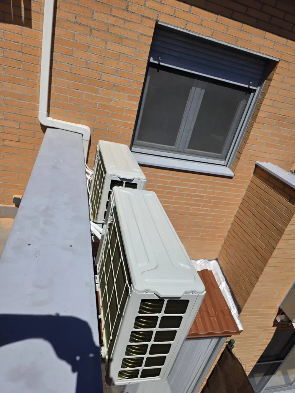 Unidades de aire acondicionado instaladas en un edificio de ladrillo, debajo de una ventana con rejas.